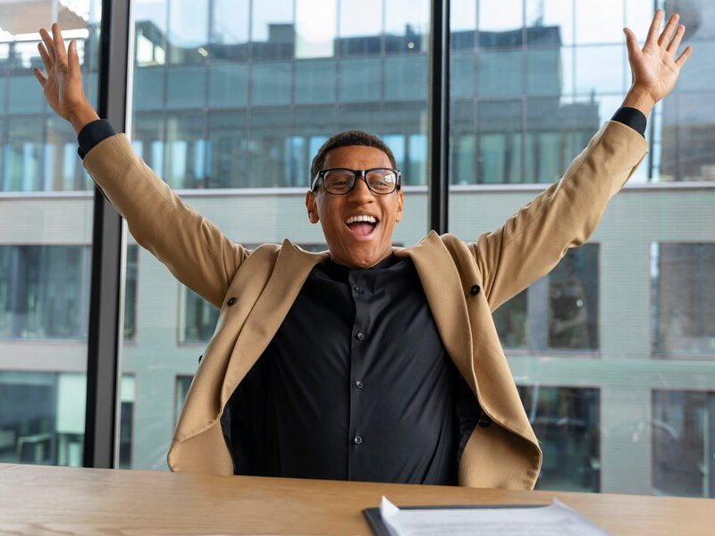 A confident Black man holding an alarm clock in one hand and giving a thumbs-up with the other, standing in front of a wall with sticky notes, symbolizing personal effectiveness and time management.